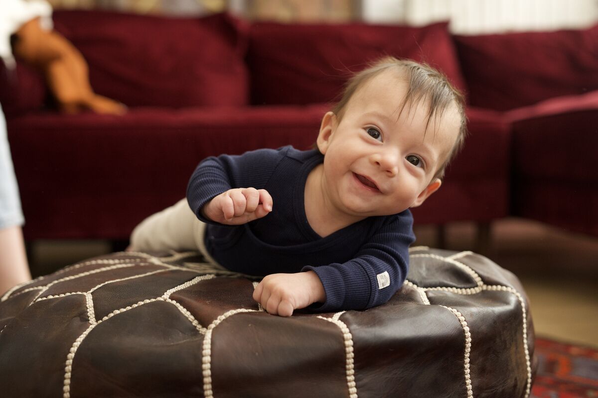 Baby smiling while leaning on a leather pouf