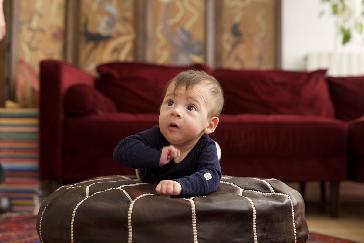 Curious baby leaning over a leather pouf